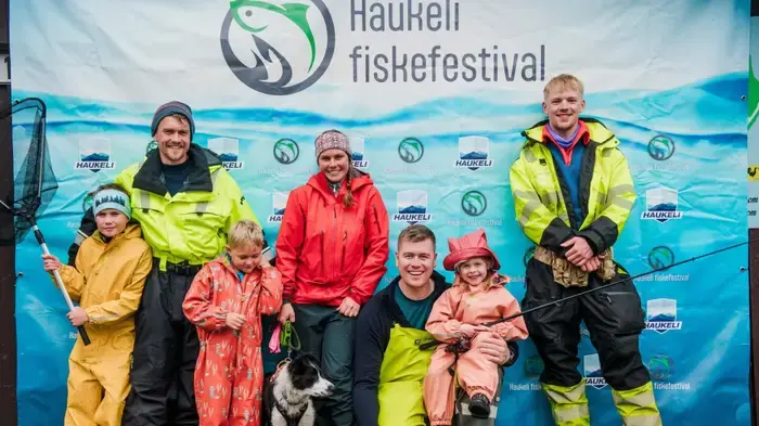 Familiar i regntøy framfor plakatveggen til Haukeli fiskefestival